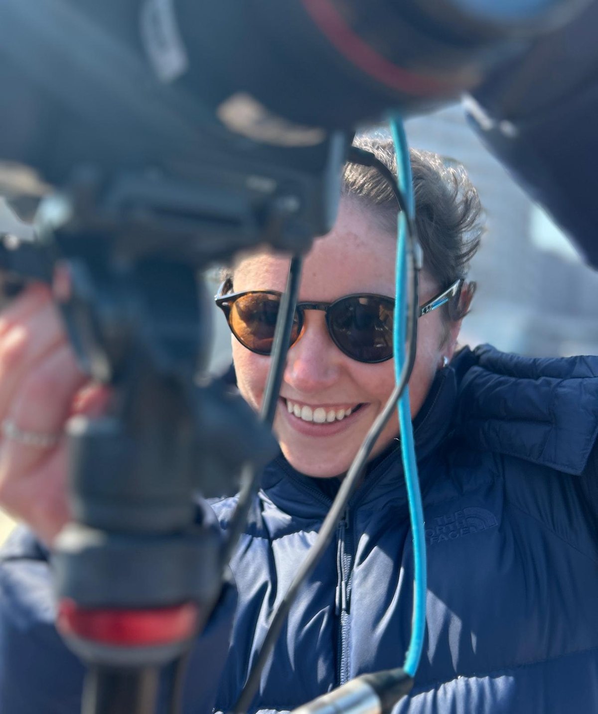 Aoife Kane smiling behind a camera on a tripod
